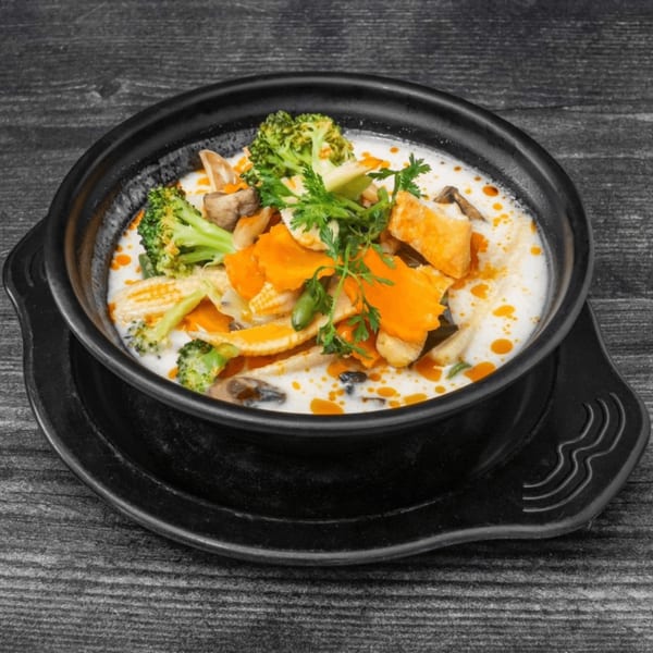 Creamy Thai soup with broccoli, carrots, mushrooms, and baby corn in a black bowl.