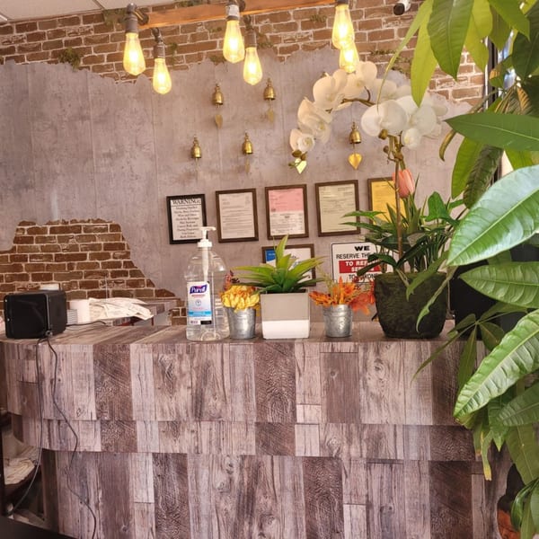 Thai Recipe Cuisine's reception desk with plants, hand sanitizer, and decorative bells on a brick and concrete wall.
